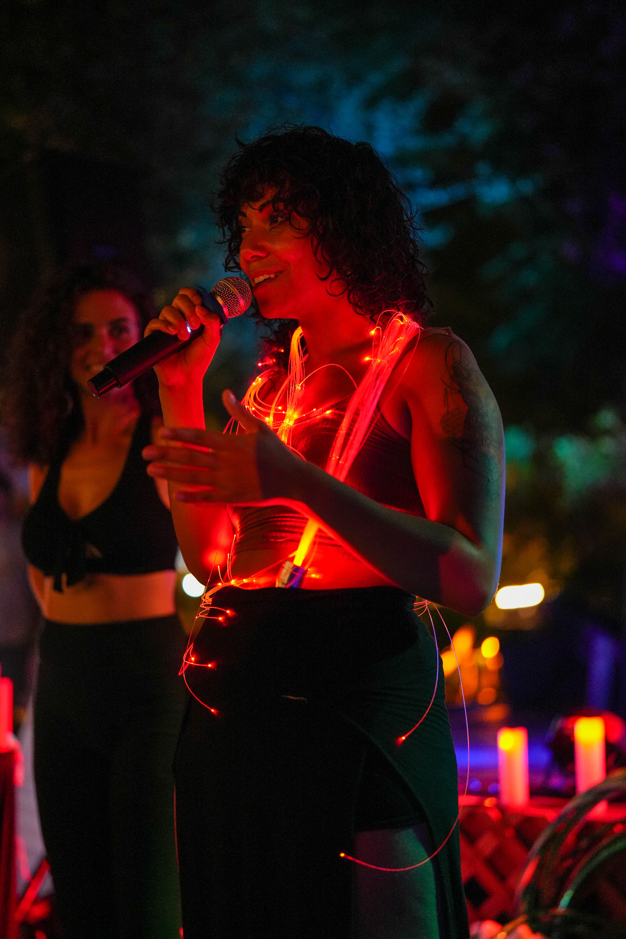 Luna Chi speaking into a microphone, draped in glowing red LED light strands
