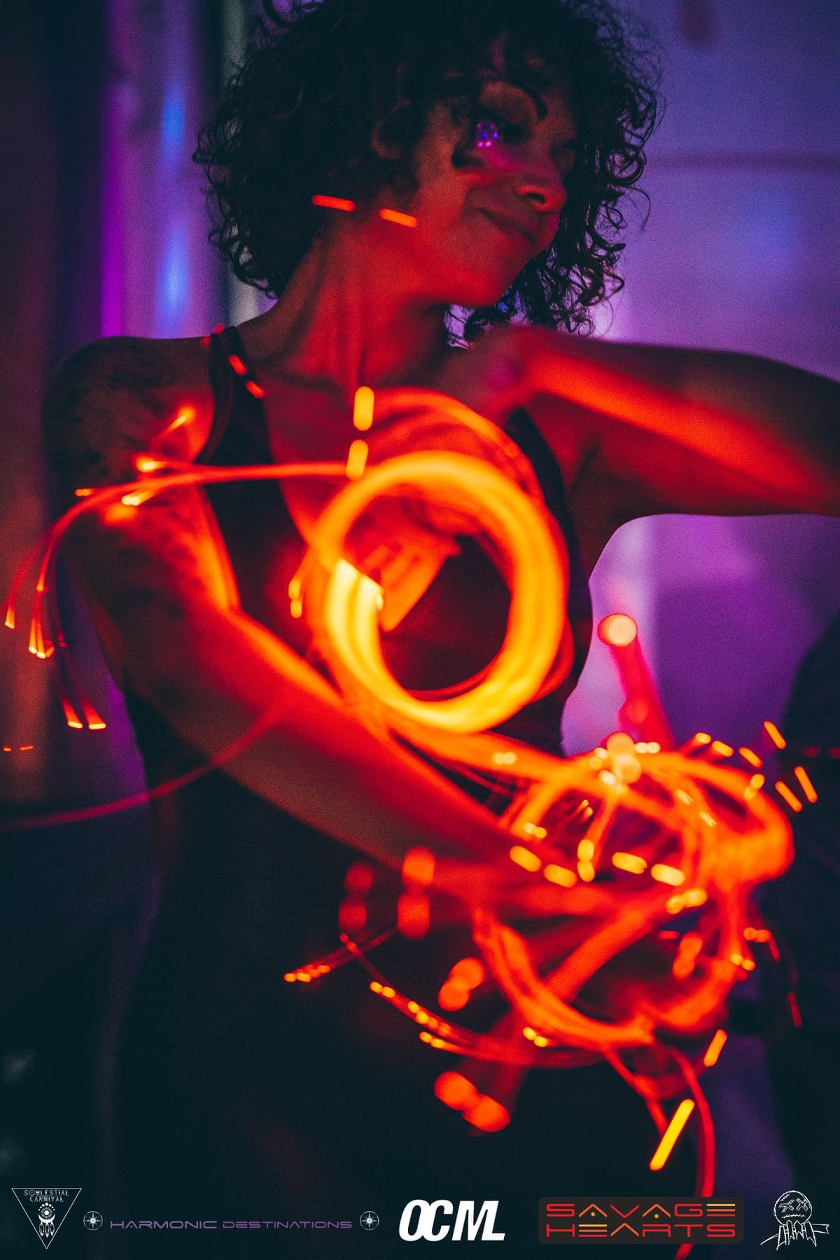 Dancer wrapped in glowing orange and red LED whip light, mid-flow